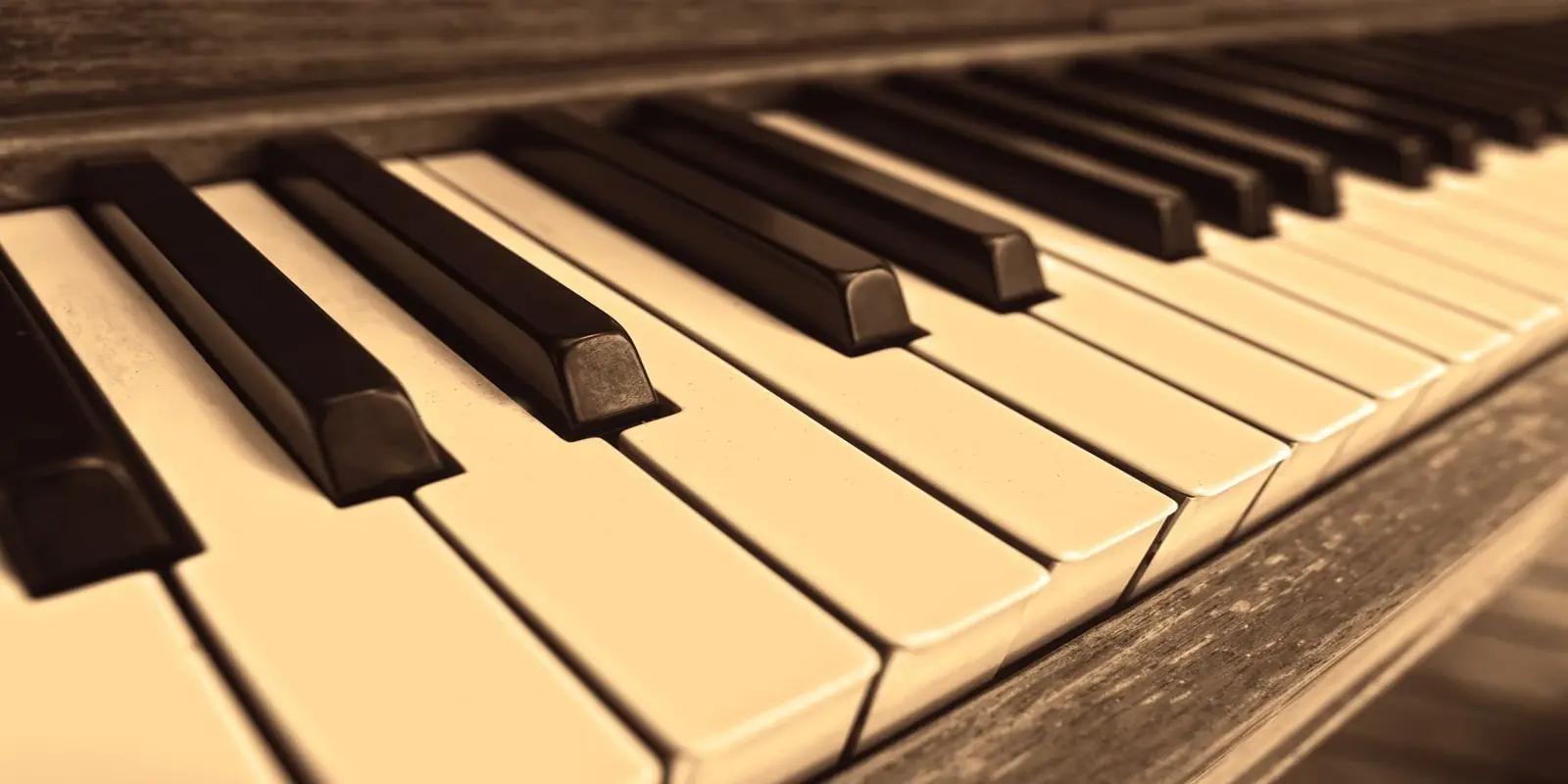 Close-up of piano keyboard showing black and white keys in warm sepia tone lighting.