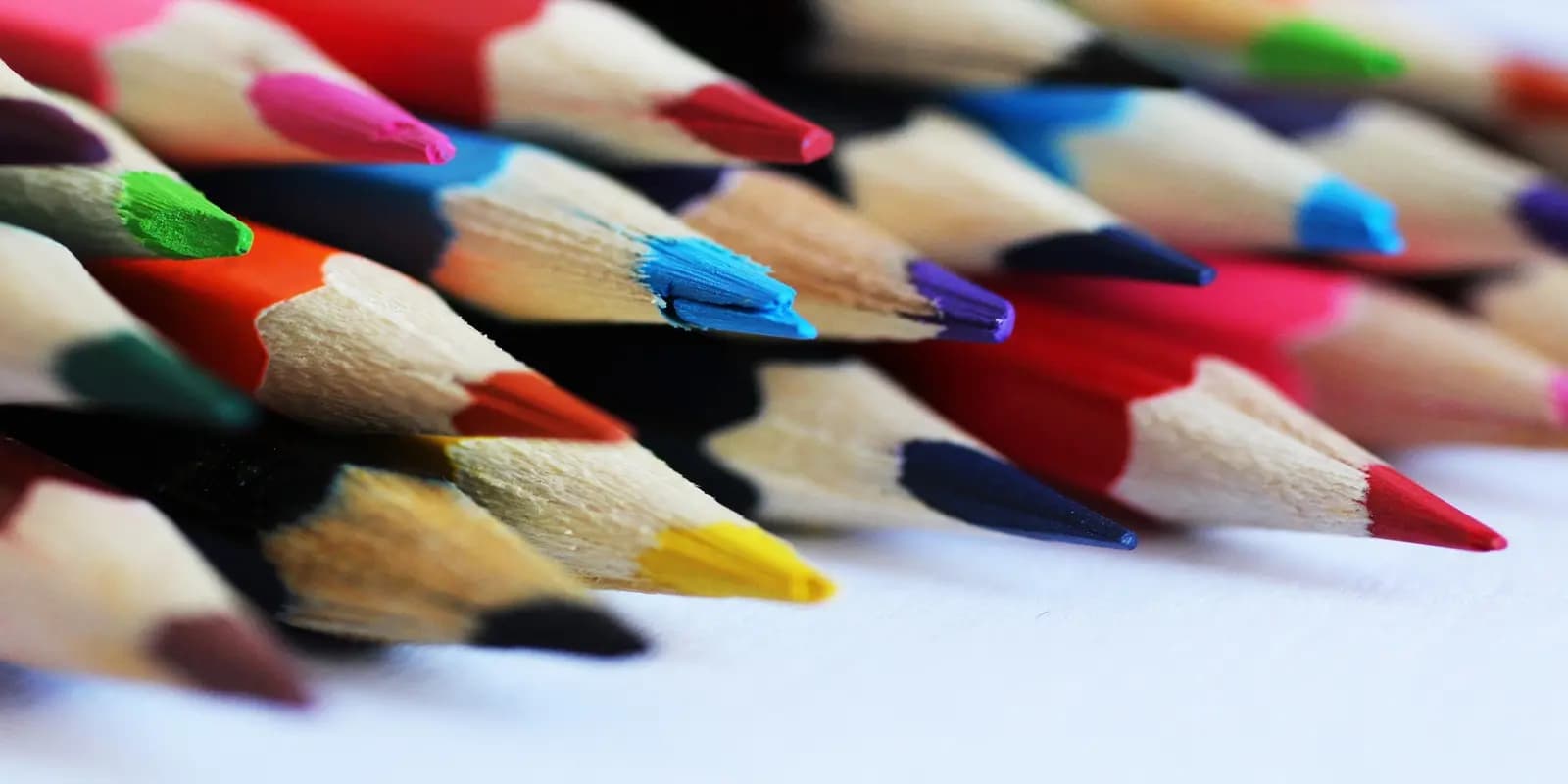 Close-up of colorful pencils arranged with tips pointing forward showing various hues on white surface.