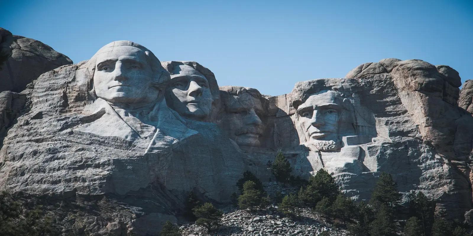 Mount Rushmore National Memorial showing carved presidential faces in granite mountain under blue sky.