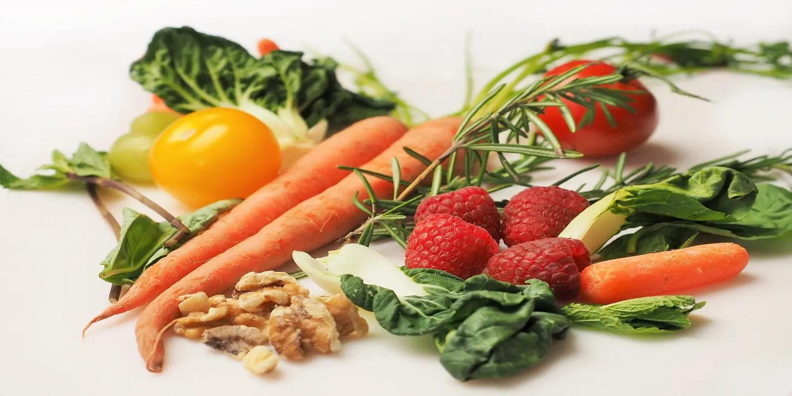 Fresh vegetables and fruits arranged together including carrots, tomatoes, leafy greens and berries.