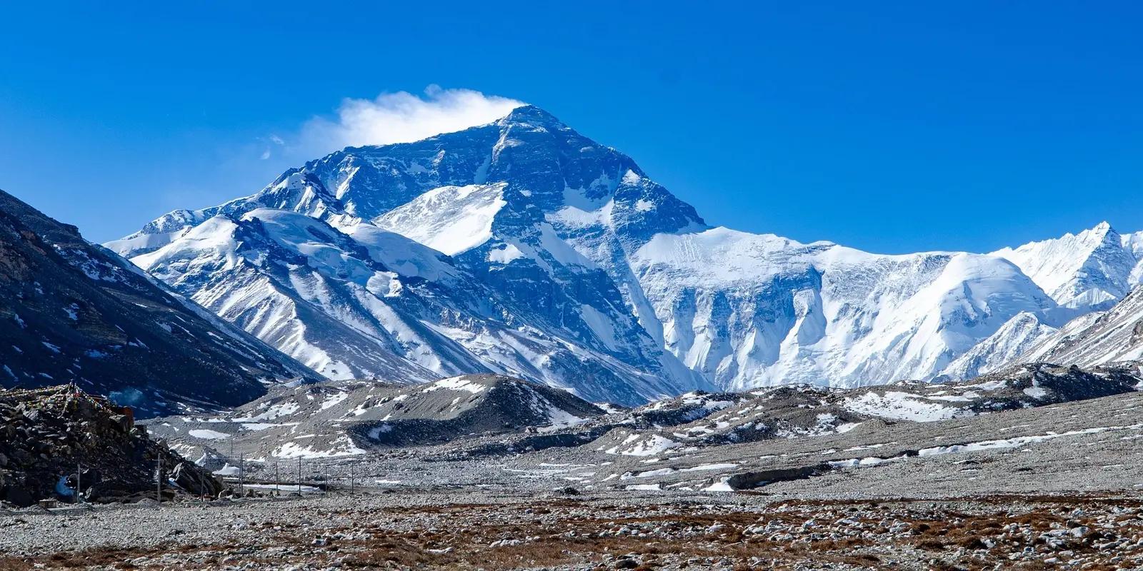 Mount Everest summit covered in snow with dramatic mountain range view against clear blue sky.