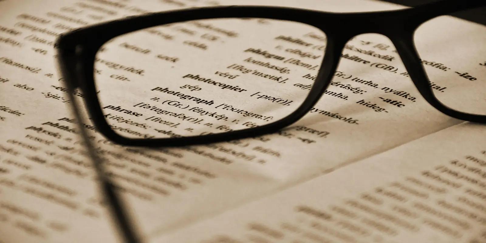 Reading glasses placed on open dictionary or reference book with text visible beneath.