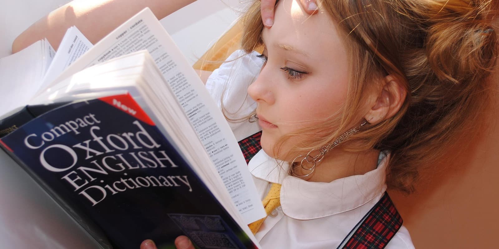 A young student in school uniform reading a Compact Oxford English Dictionary.