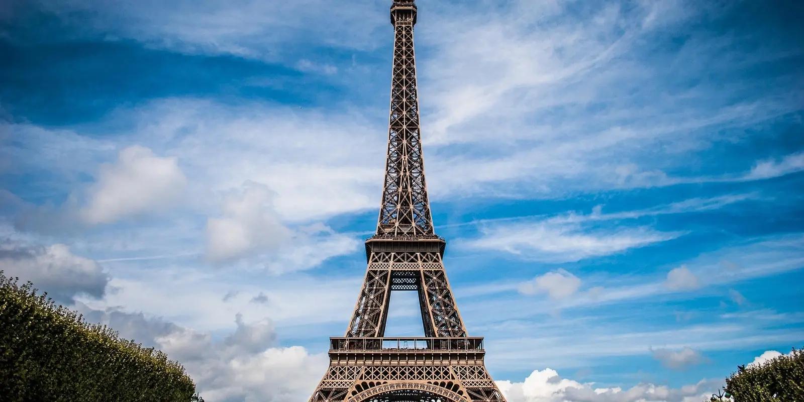 The Eiffel Tower in Paris, France, under a blue sky with clouds, showcasing its iconic iron lattice structure.
