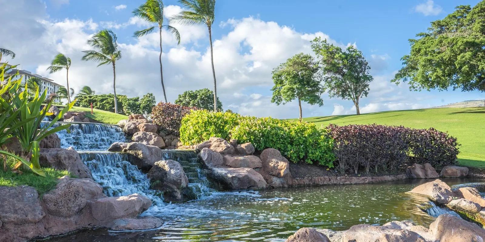 Tropical waterfall feature with palm trees and lush landscaping at Hawaii Oahu resort golf course.
