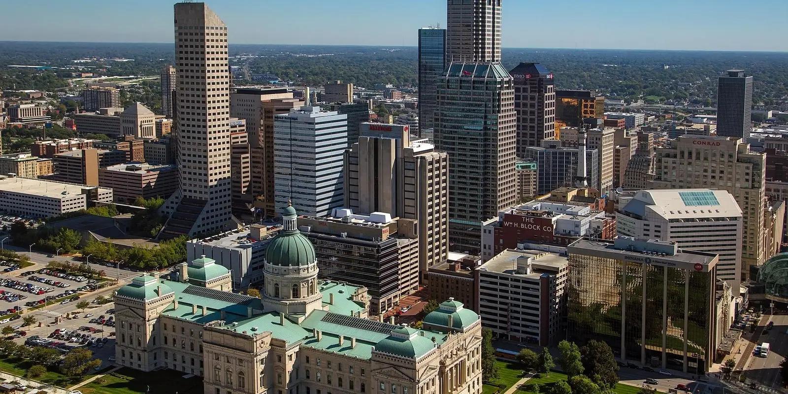 Aerial view of downtown Indianapolis, Indiana showing the State Capitol building with its distinctive green dome in the foreground and modern skyscrapers in the background.