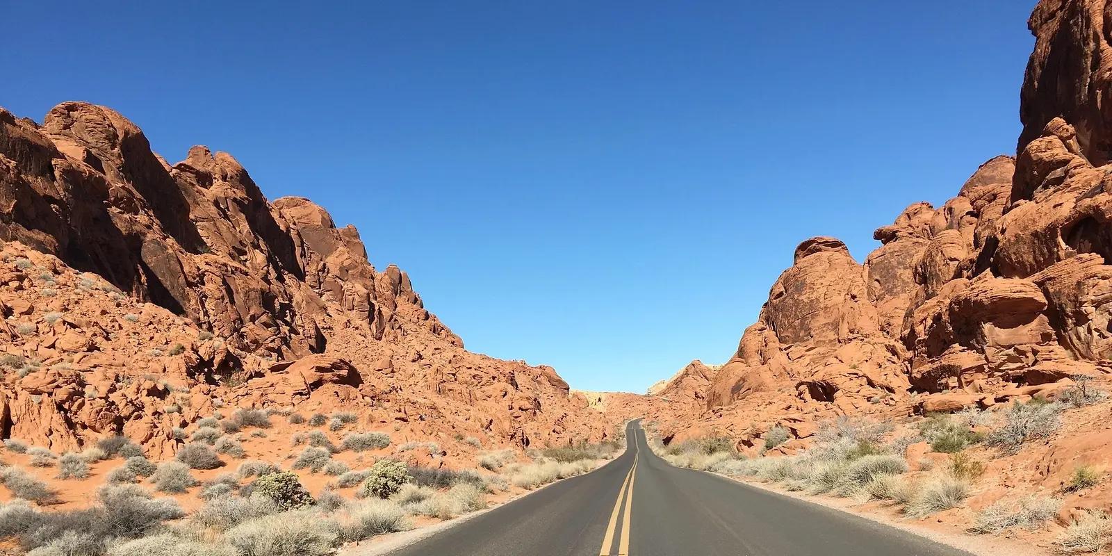 Scenic desert road through red rock formations under a clear blue sky in Nevada.