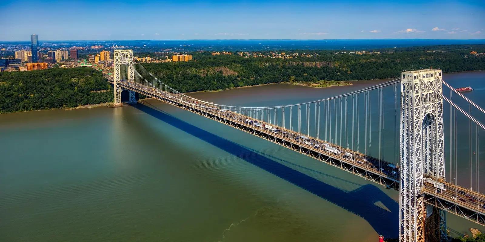 Aerial view of the George Washington Bridge spanning the Hudson River, connecting New York and New Jersey, with a city skyline in the background.