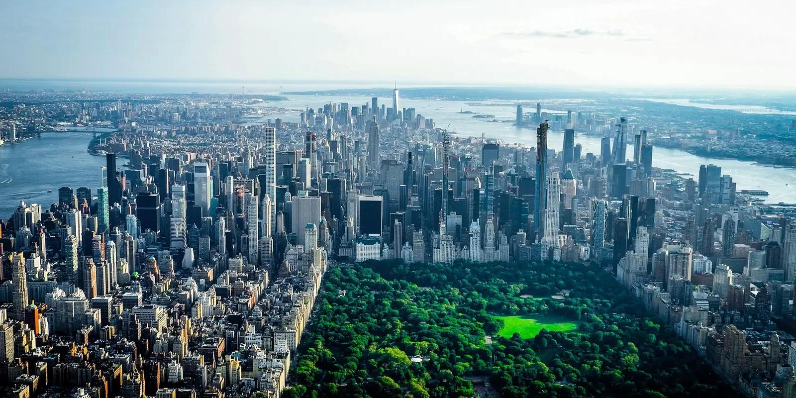 Aerial view of Manhattan skyline with Central Park's lush greenery contrasting against dense urban development, with One World Trade Center visible in the distance.
