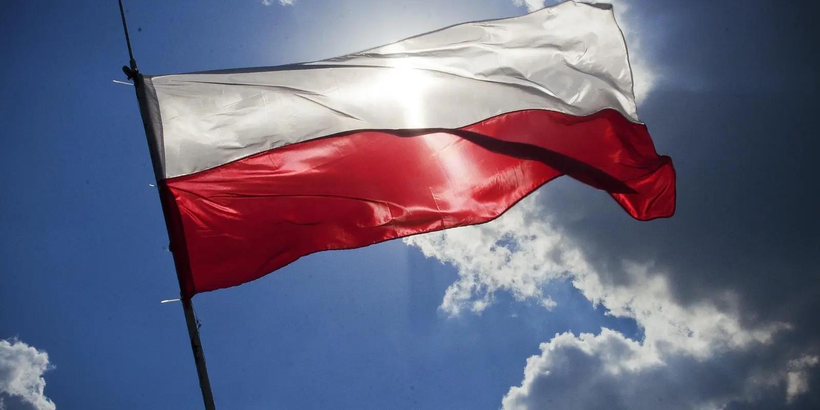 Polish flag waving against blue sky with sunlight shining through the fabric.