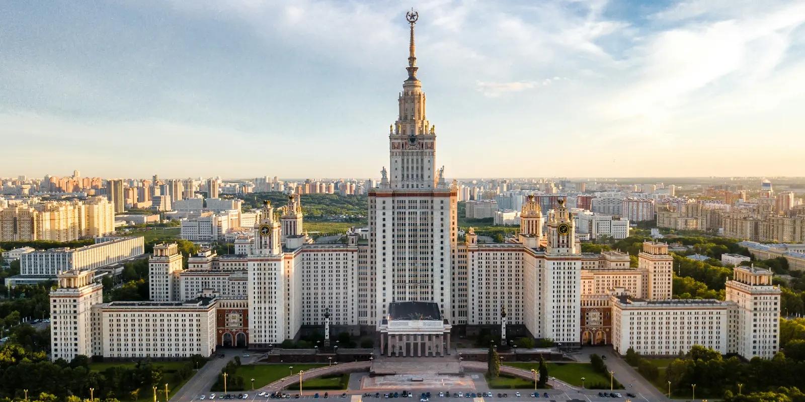 Aerial view of Moscow State University's main building with its distinctive Stalin-era skyscraper architecture featuring a tall spire and symmetrical wings against the Moscow cityscape.