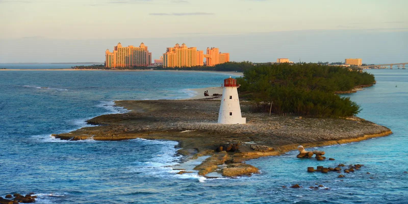 Paradise Island Lighthouse in Nassau, Bahamas, featuring a white lighthouse on a rocky island with turquoise water surrounding it, and the Atlantis resort in the distance.