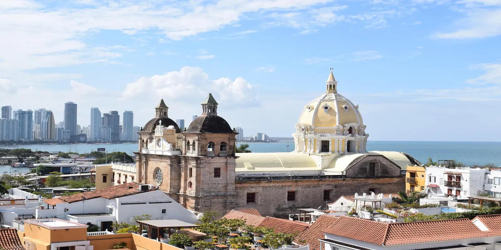 Cartagena, Colombia, featuring the Cartagena Cathedral with its yellow dome and bell towers, surrounded by colorful buildings and the city skyline in the background.