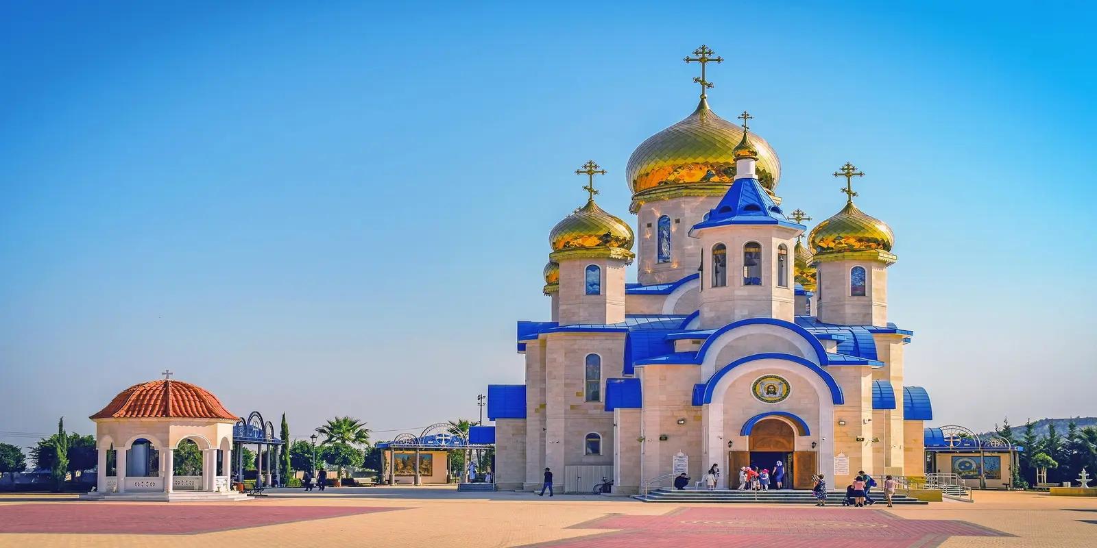 The St. Nicholas Russian Orthodox Church in Limassol, Cyprus, featuring golden domes, blue accents, and a white facade against a clear blue sky.