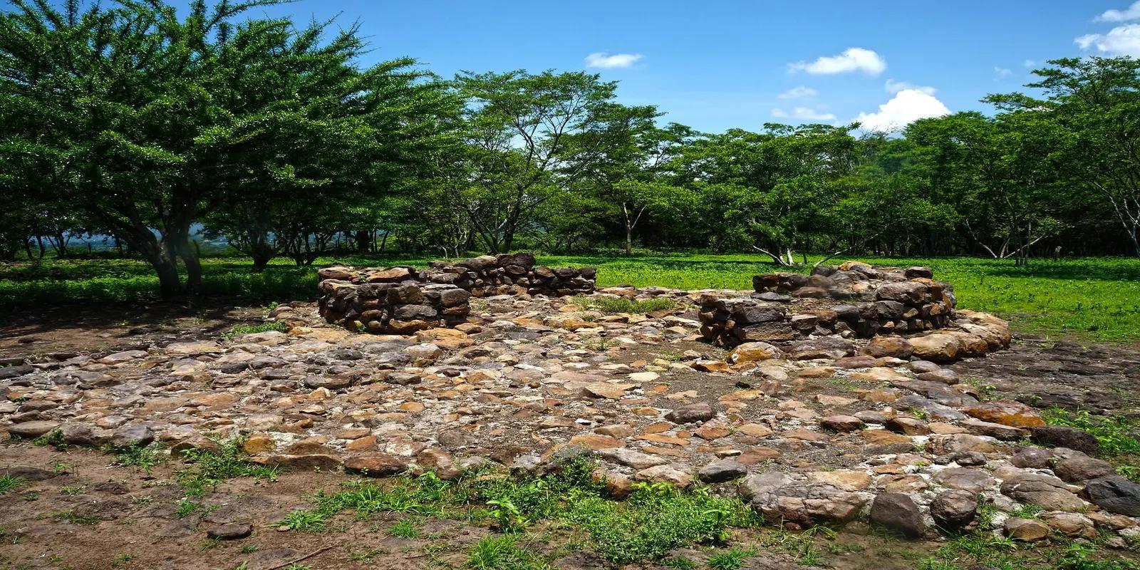 The archaeological site of Tazumal in El Salvador, featuring ancient stone ruins amidst a lush green landscape with trees.
