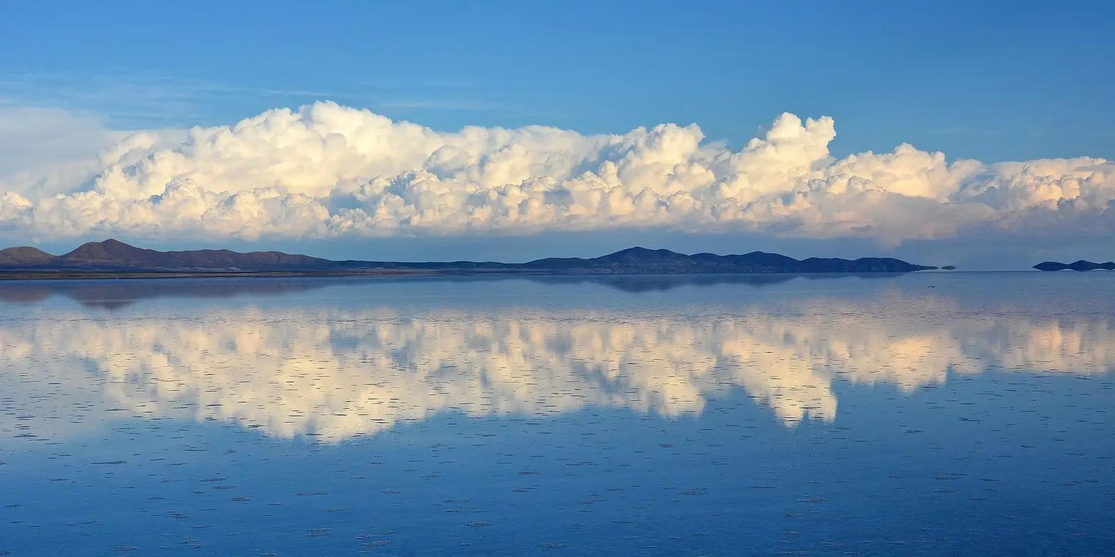 Salar de Uyuni, Bolivia, featuring a vast salt flat with a mirror-like reflection of the sky and clouds on the water's surface.