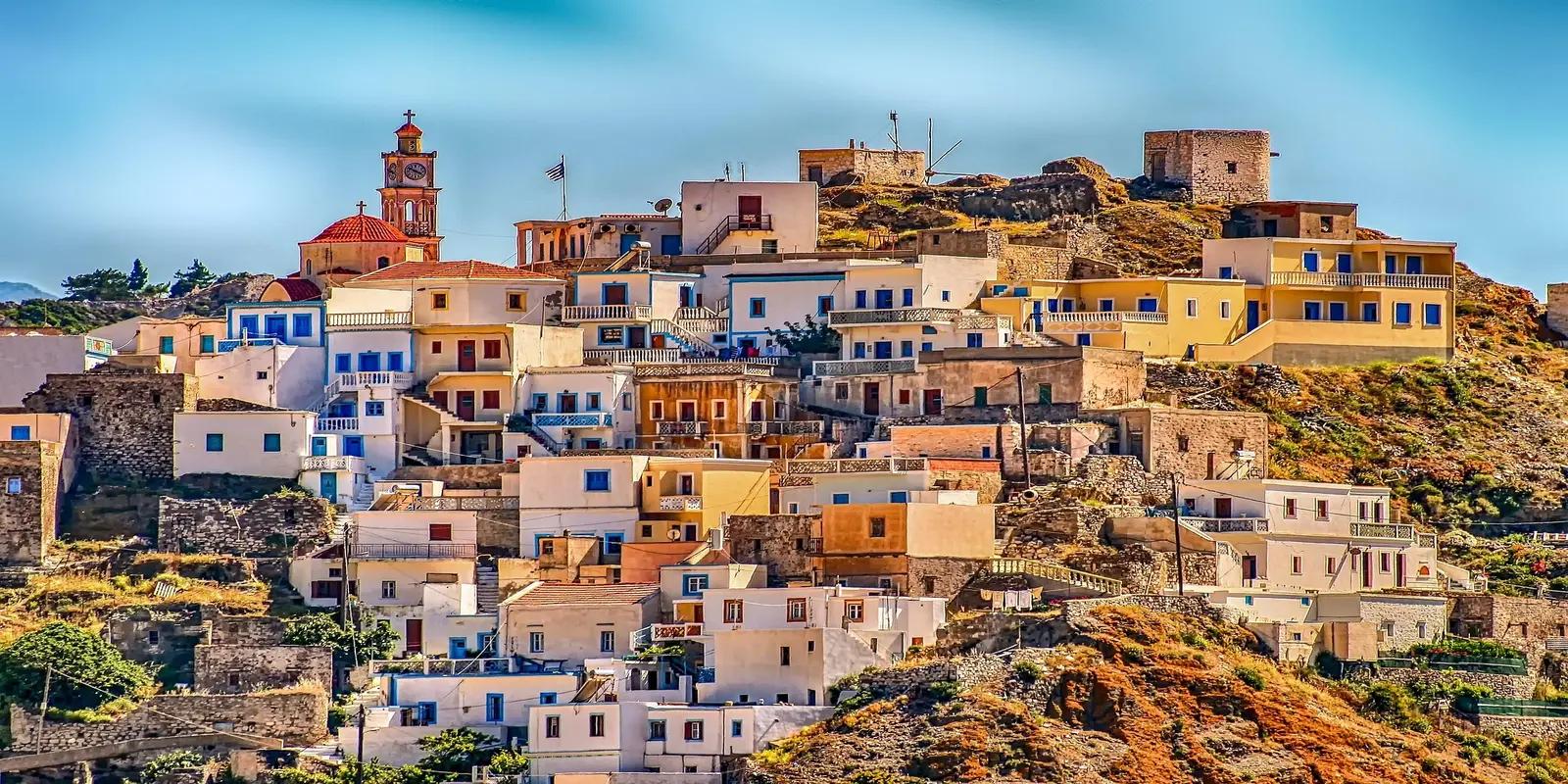 Scenic view of a village in Karpathos, Greece, featuring colorful houses nestled on a hillside with a clock tower and a ruined fortress.
