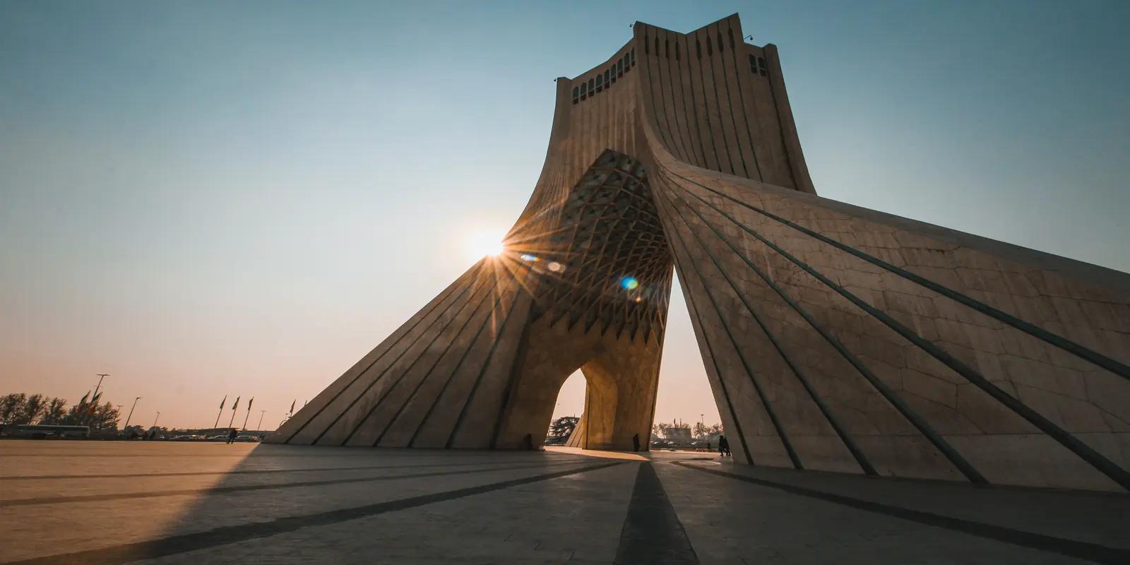 The Azadi Tower in Tehran, Iran, featuring its iconic modern architecture with a sunburst effect shining through its central arch.