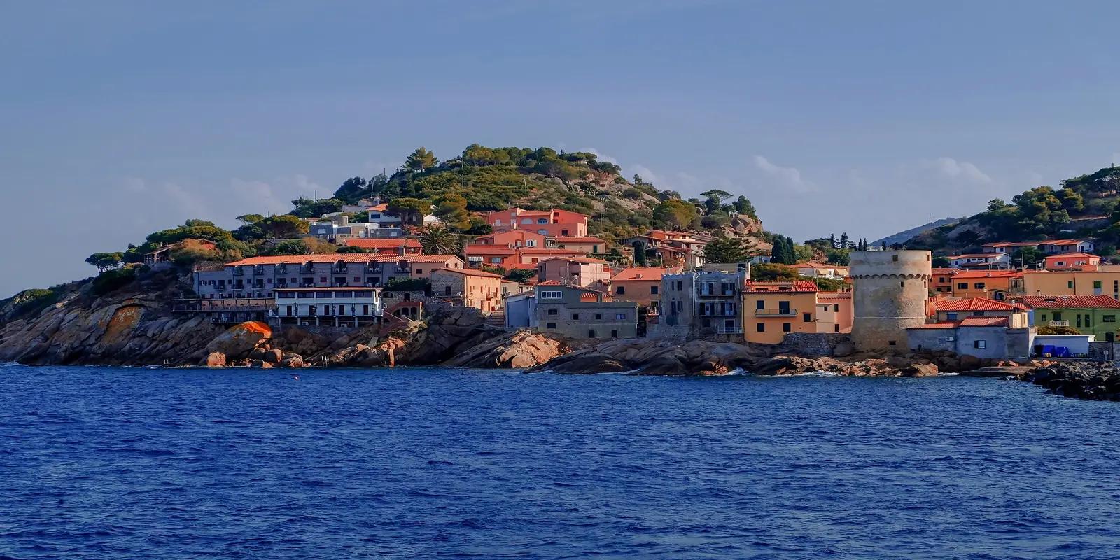 Giglio Porto, Italy, featuring colorful buildings nestled on a rocky hillside overlooking the deep blue sea.