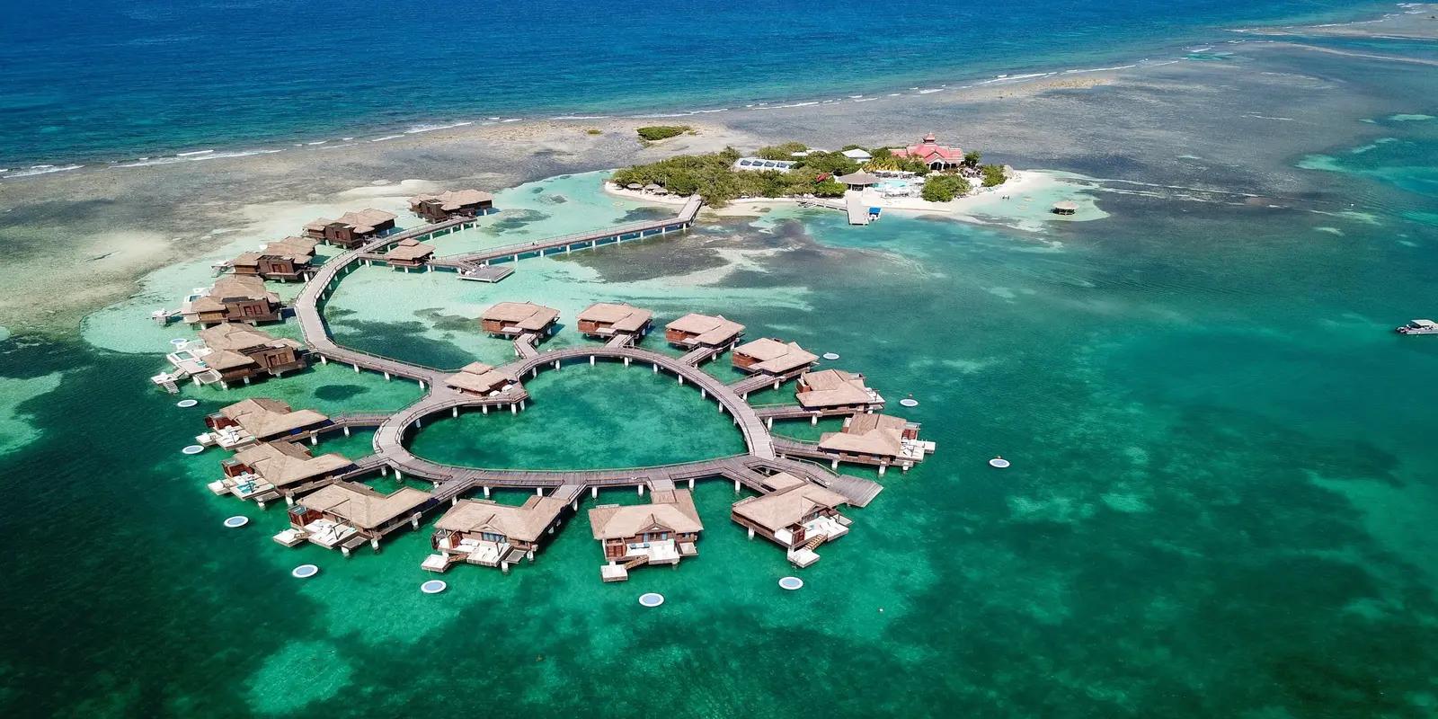 Aerial view of Sandals South Coast resort in Jamaica, featuring overwater bungalows arranged in a heart shape, surrounded by clear turquoise water.
