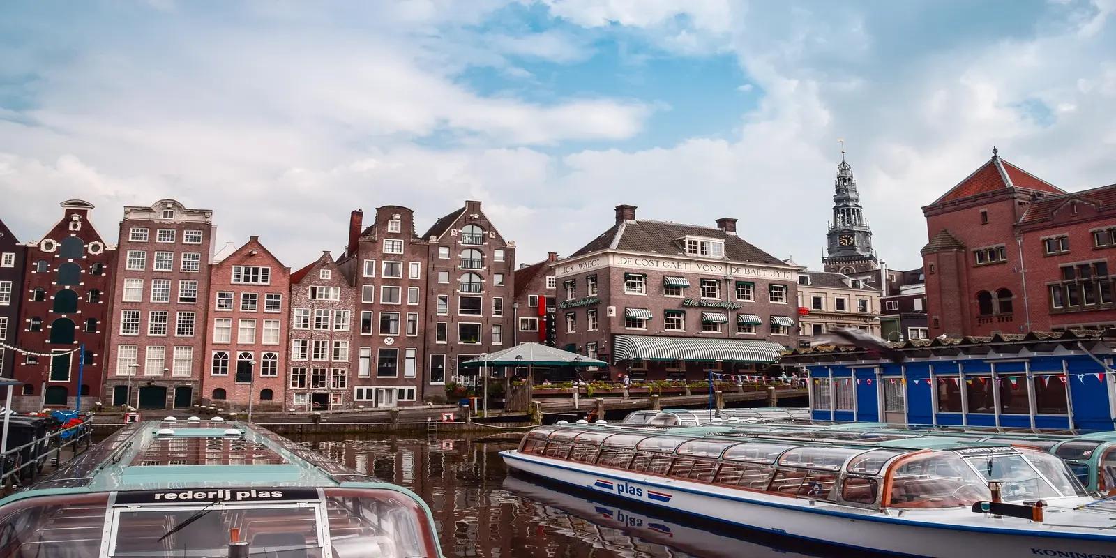 Canal boats and traditional Dutch buildings in Amsterdam, Netherlands, with a church tower in the background.