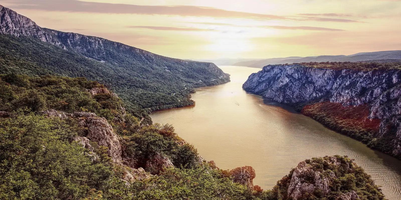 Scenic view of Djerdap National Park, Serbia, featuring the Danube River flowing through a gorge between steep cliffs covered in lush vegetation.