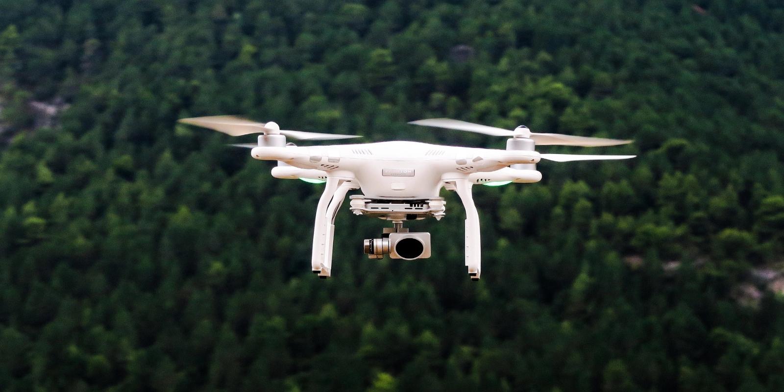 A white DJI Phantom 4 Pro drone flying in the air with a camera mounted underneath.