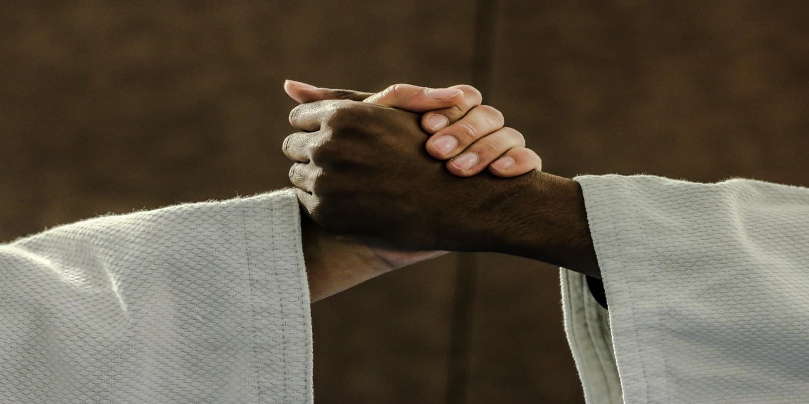 Close-up of two hands clasped together in a sign of respect or sportsmanship, wearing white martial arts uniforms.