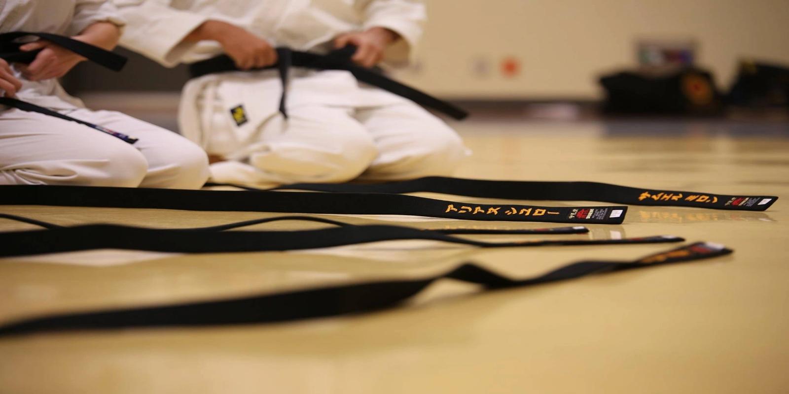 Several black belts with embroidered text laid out on a light-colored floor in a martial arts training hall.