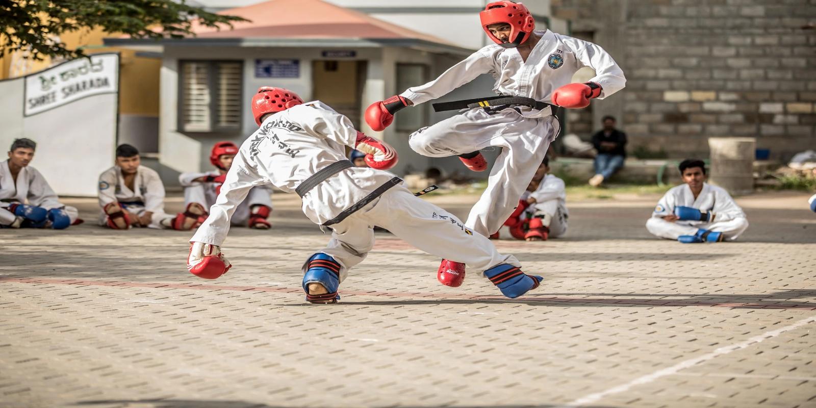 Two taekwondo practitioners in white uniforms and protective gear engaged in a sparring match.
