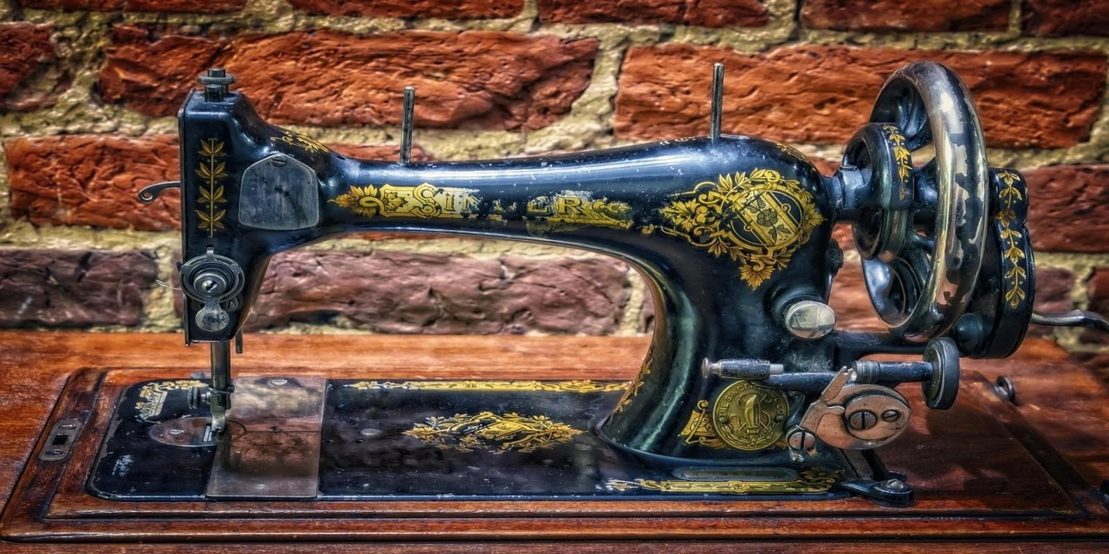 A detailed image of an ornate, black and gold antique Singer sewing machine sitting on a wooden surface in front of a brick wall.