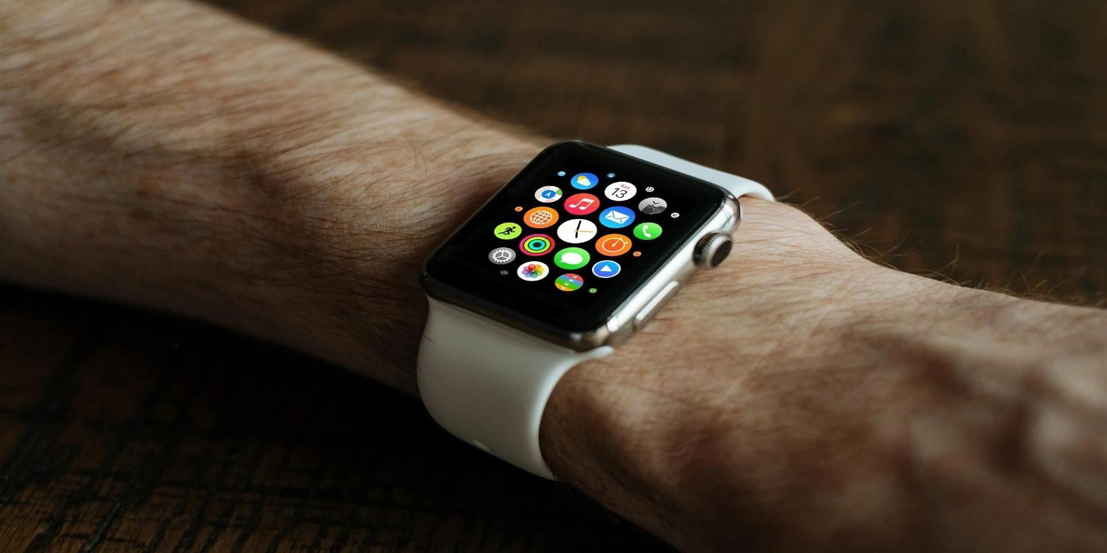 A close-up of an Apple Watch with a white band, displaying a colorful app interface on its screen.