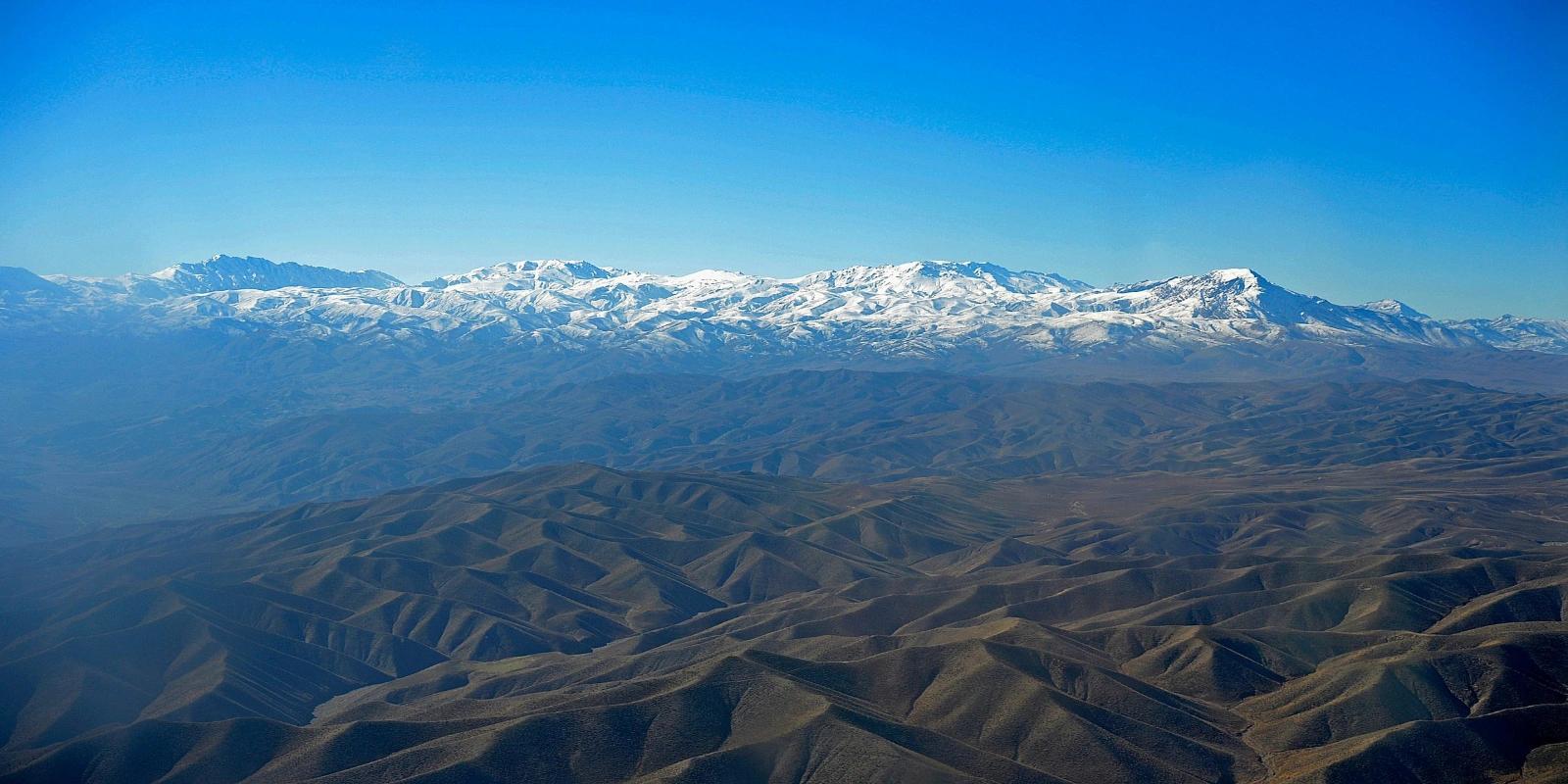 Snow-capped Hindu Kush mountains towering over arid foothills in Afghanistan, showcasing the country's dramatic landscape.