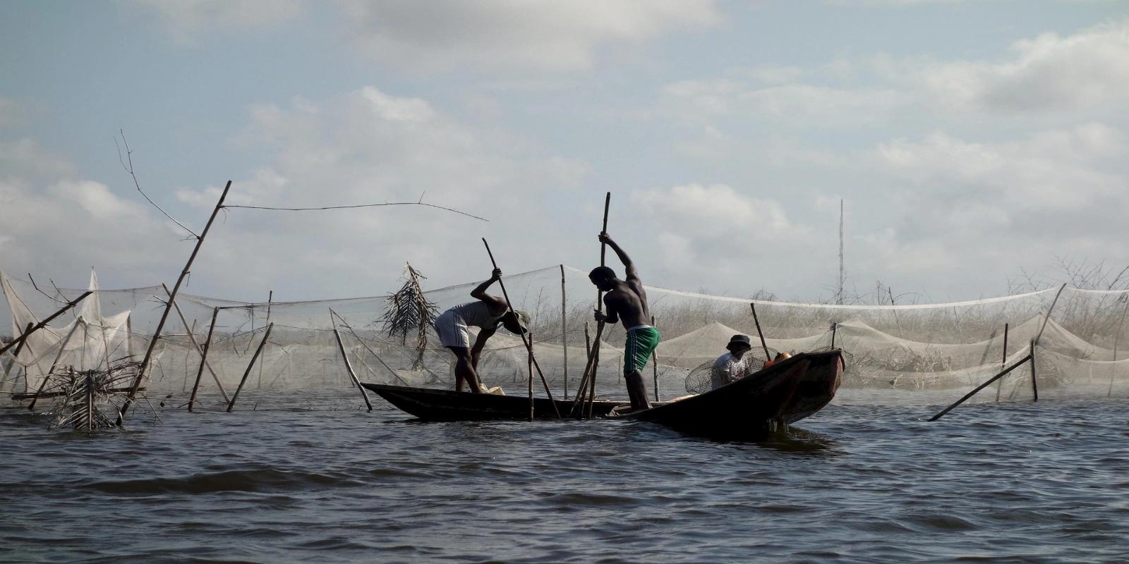 Beninese fishermen in a traditional wooden boat with fishing nets on a lake in Benin, depicting local fishing practices.
