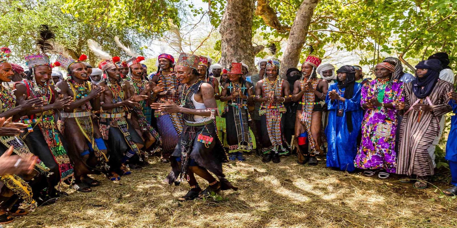 Chadian people in vibrant traditional attire and ornate makeup performing a cultural dance during the Guérewol festival in Chad.