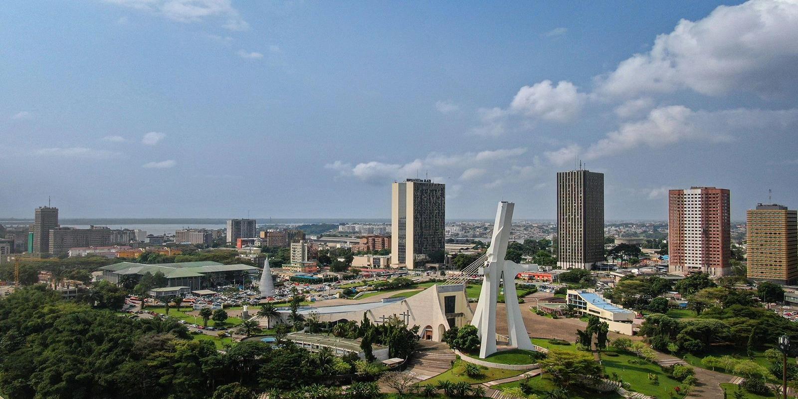 Modern skyline of Abidjan, Cote d'Ivoire, featuring high-rise buildings and the iconic, architecturally unique St. Paul's Cathedral.