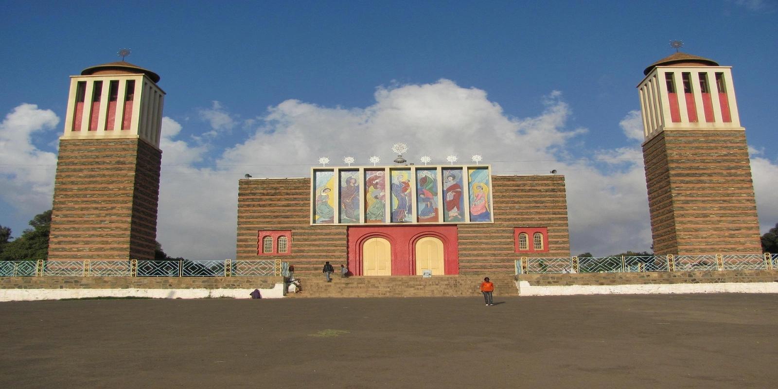The Enda Mariam Orthodox Cathedral in Asmara, Eritrea, displaying its distinctive striped twin towers and vibrant facade murals under a blue sky.