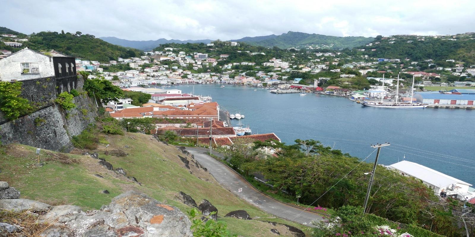 Scenic overlook of St. George's harbor, Grenada, revealing its colorful waterfront buildings, moored boats, and lush green surrounding hillsides.