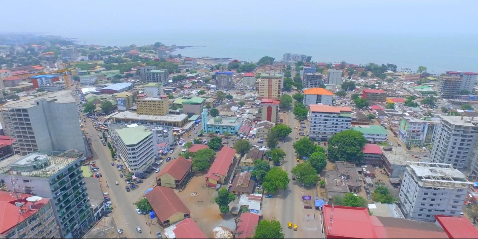 Aerial panorama of Conakry, Guinea, showcasing the densely built-up coastal capital city, including a prominent mosque, adjoining the Atlantic Ocean.