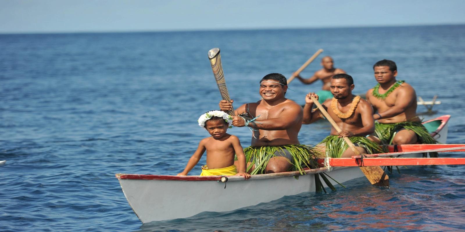 A group of Nauruan paddlers in outrigger canoes on the ocean, with one man and a child in the foreground smiling.