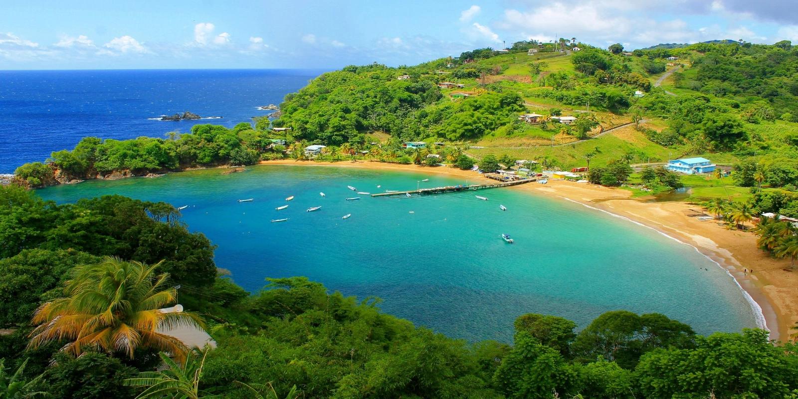 Panoramic view of Parlatuvier Bay in Tobago, Trinidad and Tobago, showing a beautiful turquoise bay with boats, a sandy beach, and lush green hillsides dotted with houses.