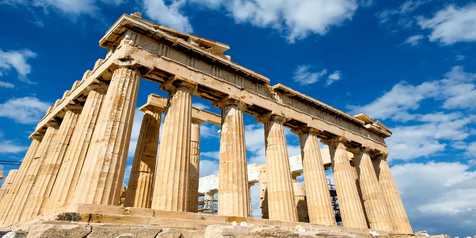 Ancient Greek Parthenon temple with classic columns on Acropolis hill against blue sky with clouds.