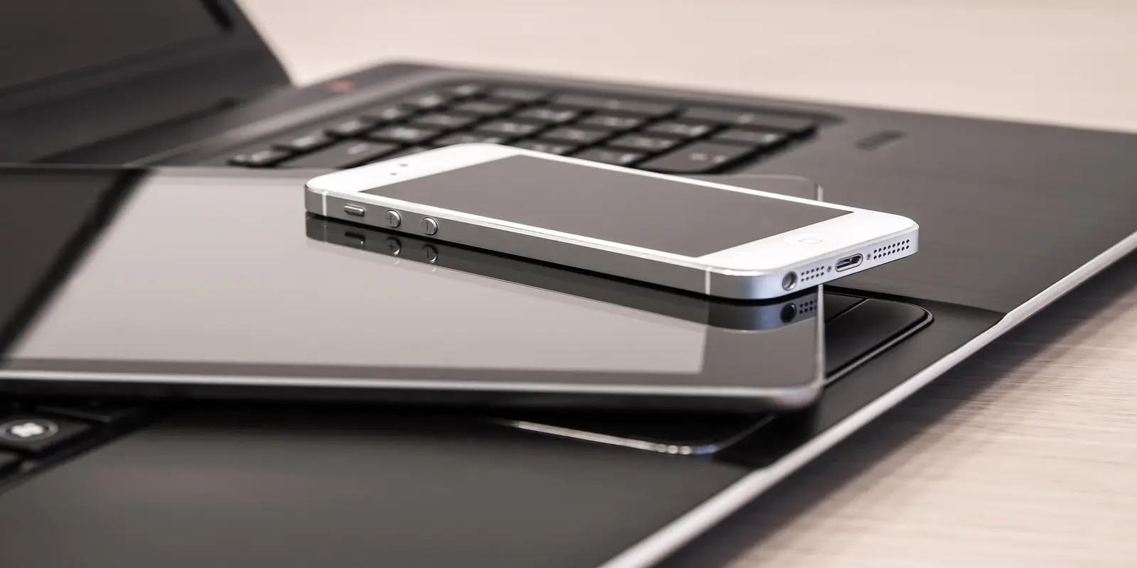 White smartphone (iPhone) resting on silver laptop keyboard in minimal business setup.