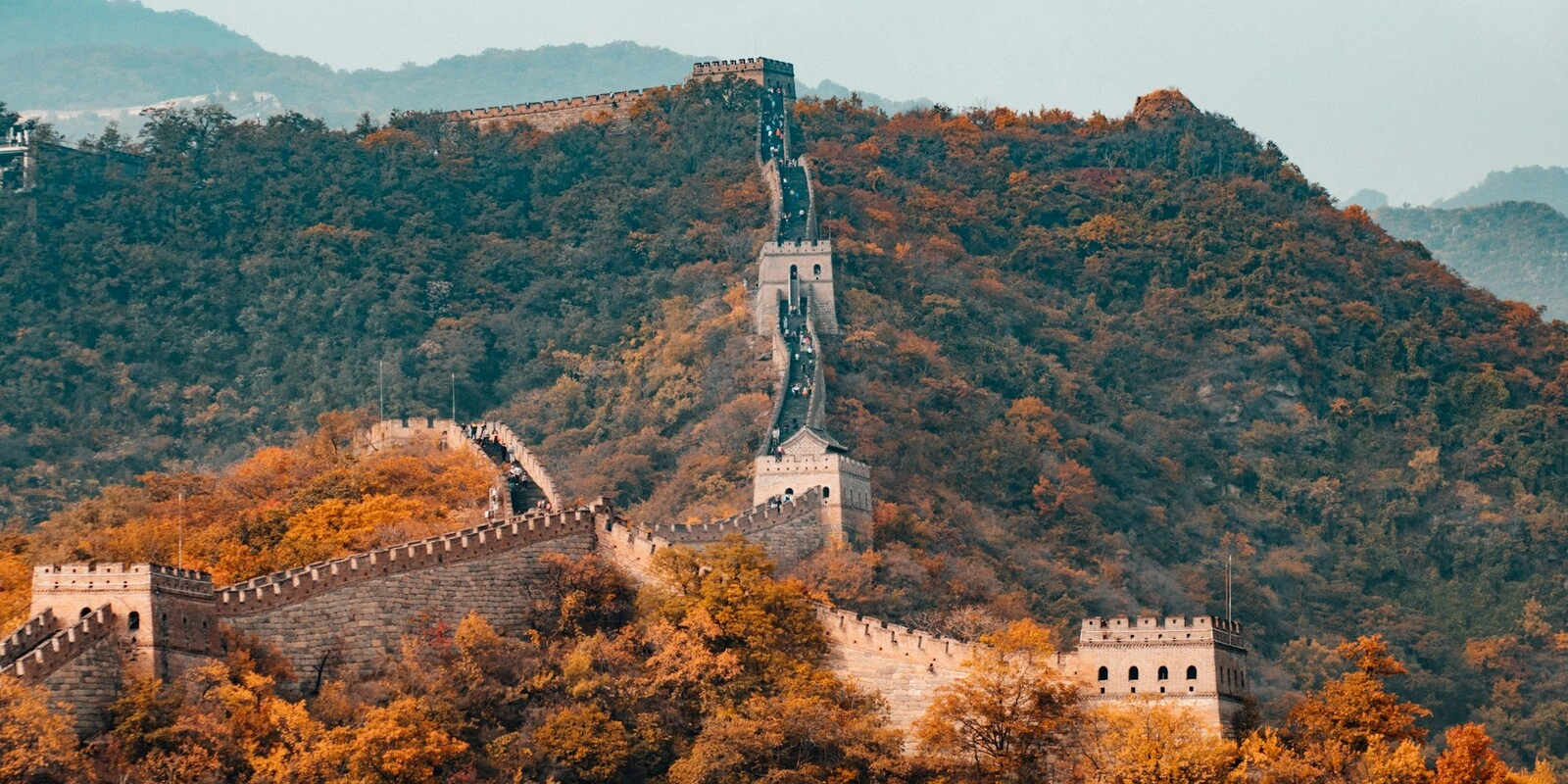 Great Wall of China winding across mountain ridges surrounded by autumn foliage.