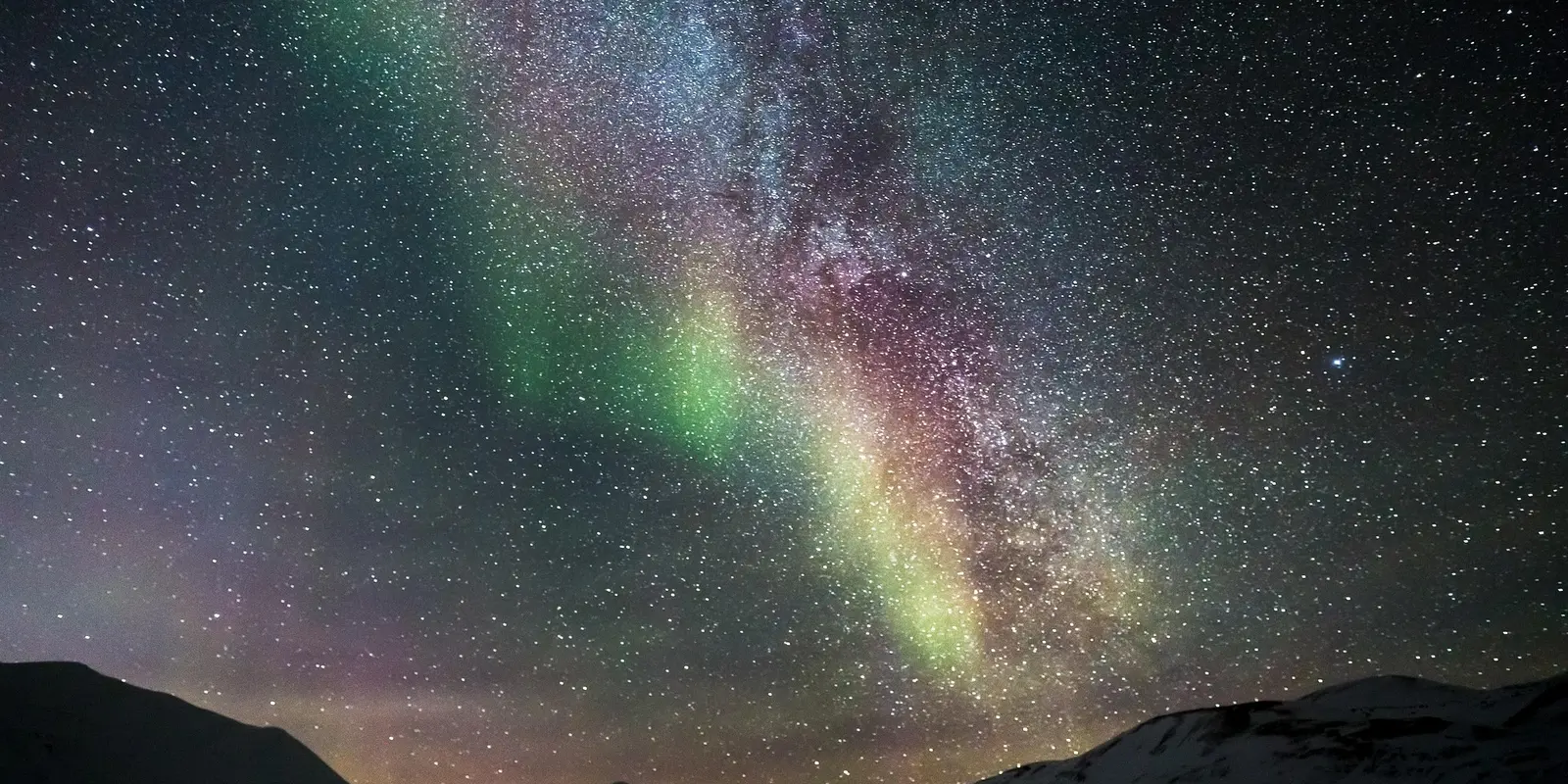 A breathtaking view of the Northern Lights illuminating the night sky with shades of green and purple over a mountainous landscape.