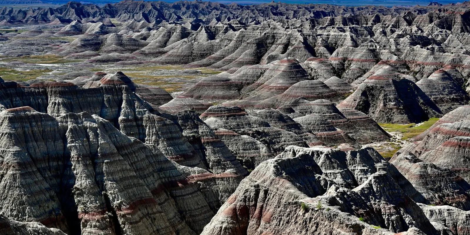 A breathtaking view of Badlands National Park, showcasing its dramatic eroded rock formations with layered sedimentary colors stretching into the horizon under a clear blue sky.