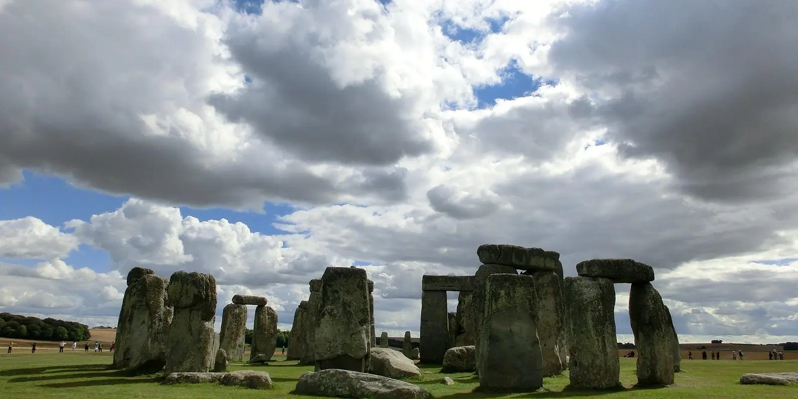 A wide view of Stonehenge, the ancient stone circle in England, set against a backdrop of a partly cloudy sky with green grass surrounding the monument.